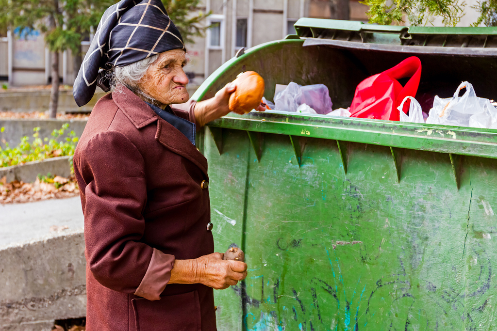 Homeless woman is searching for food in garbage dumpster. Woman in poverty is searching something in container.